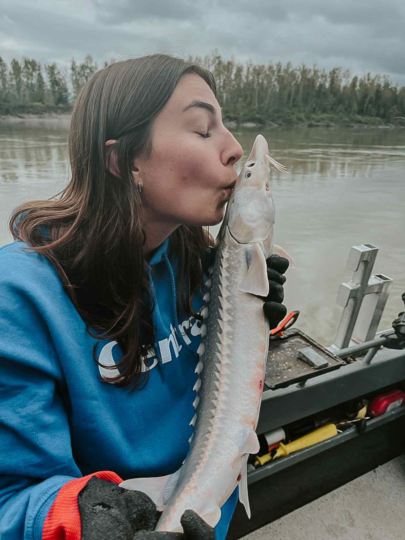 A guest kisses the nose of a small sturgeon on a boat on the Fraser River.