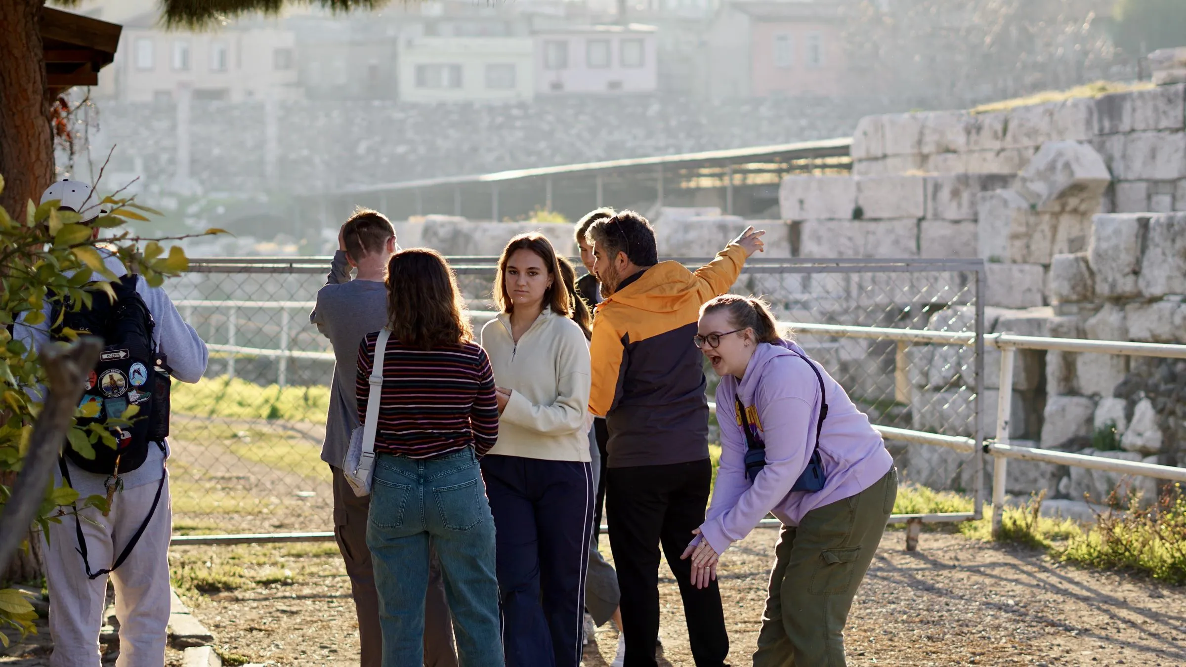 Travelers at a railing above the excavated agora of Smyrna as their guide points across the ruins