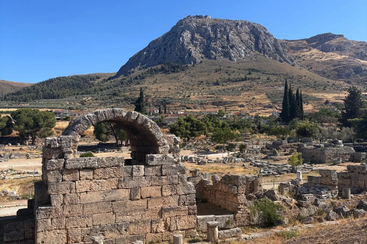 A Roman stone arch in the ruins of ancient Corinth, with the rock of Acrocorinth rising behind