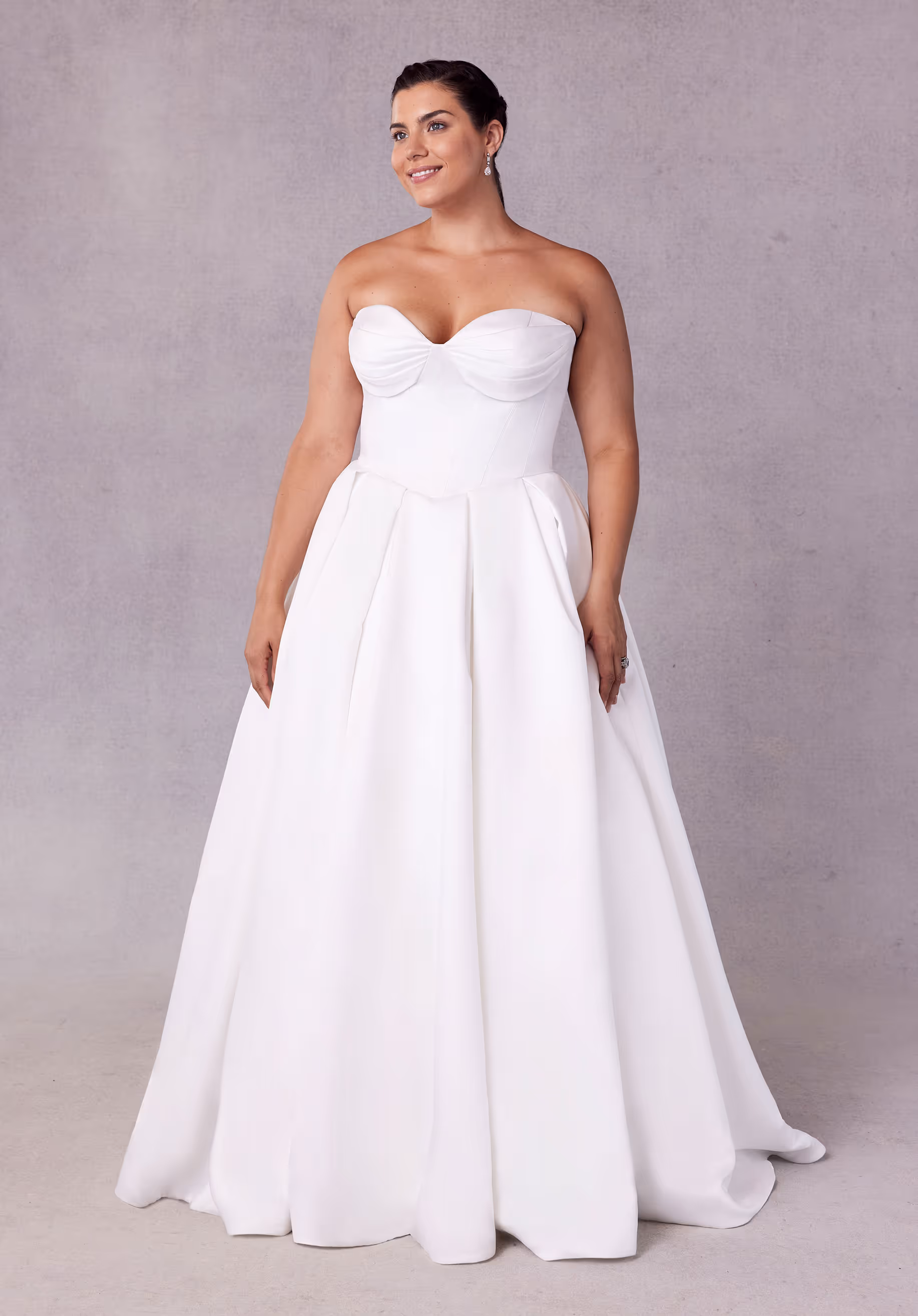 Timeless ball gown wedding dress has a sweetheart corset bodice with beaded, draped bust on a basque waist with lace-up corset back, detachable off-the-shoulder sleeves, and side bustles on a box-pleated satin skirt.
