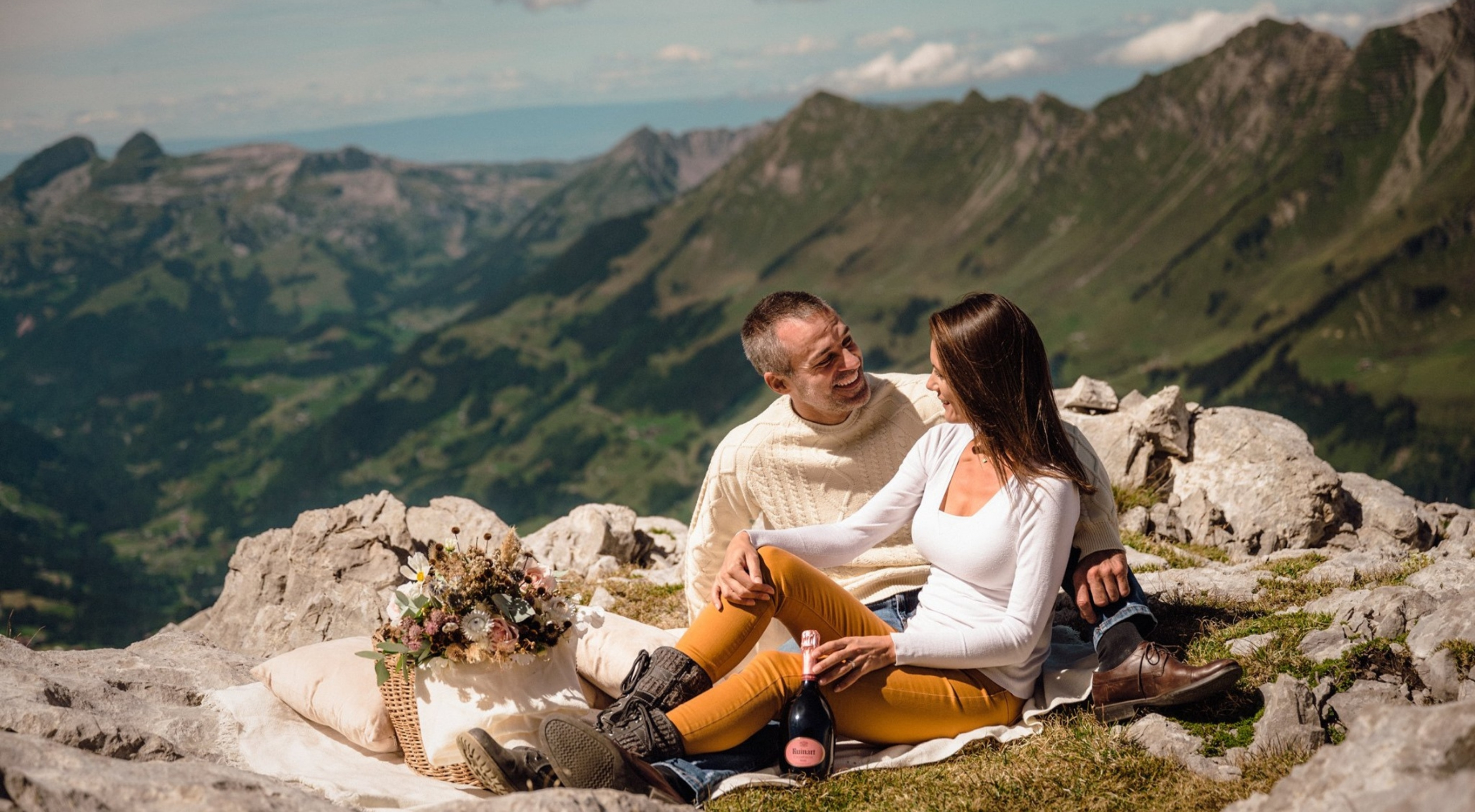 Photo of a couple on top of a mountain enjoying the view of the surrounding Alps