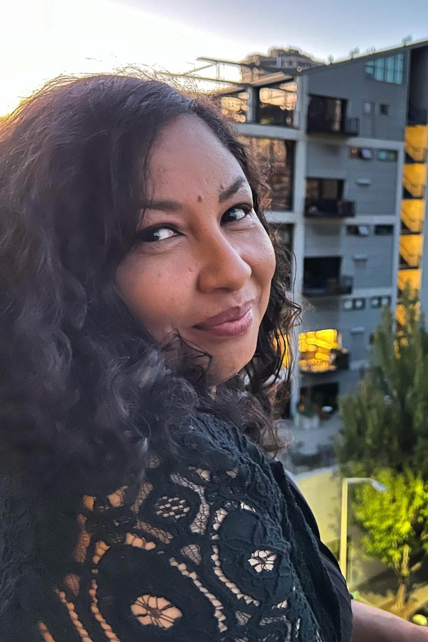 Ms Leanne, Productions Dance faculty, smiling over her shoulder on a Seattle balcony at sunset.