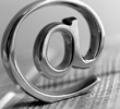 Shiny metallic at symbol (@) with a blurred wooden background.