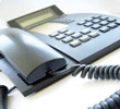 Close-up of a black office telephone with keypad and coiled cord on a white surface.