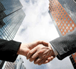 Two business people shaking hands with skyscrapers and cloudy sky in the background.