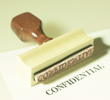 Wooden rubber stamp with the word CONFIDENTIAL inked on white paper.