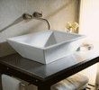 Modern white square vessel sink on dark countertop with wall-mounted faucet and light background.