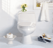Clean white toilet with vase of yellow flowers and towel hanging on wall in bright bathroom.
