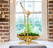 Golden balance scale on white surface in front of window with brick wall and green trees visible outside.