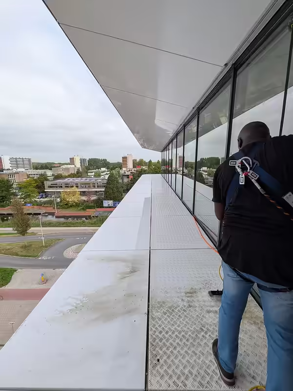 Witte gevelband met traanplaat vóór de reiniging, vervuild met groene aanslag en vuil, kantoorgebouw Gouda