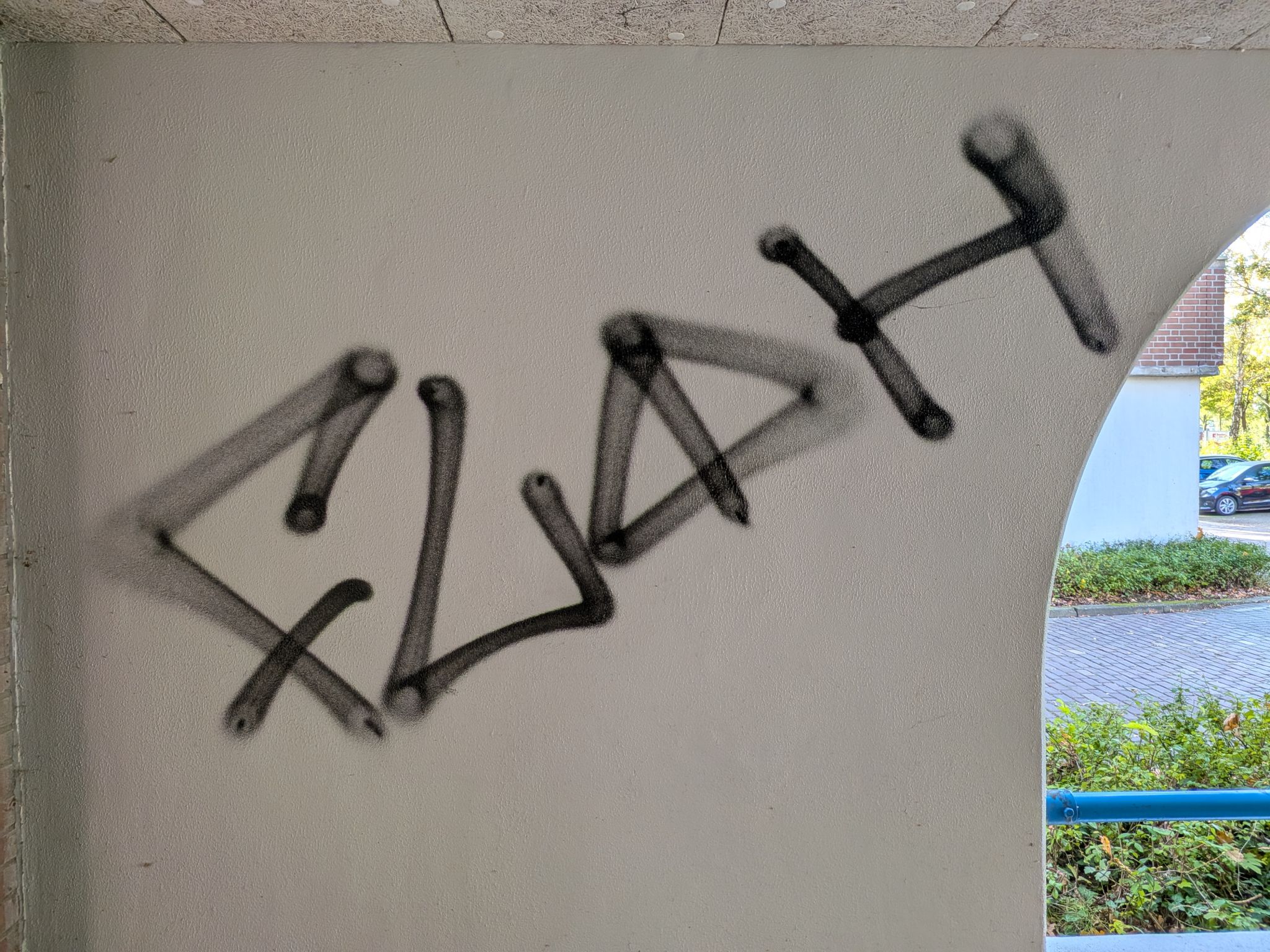 Zwarte spuitverf-graffiti op een gestuukte wand in een portiek van een VvE in Vlaardingen, vóór de verwijdering door Mattanna B.V.