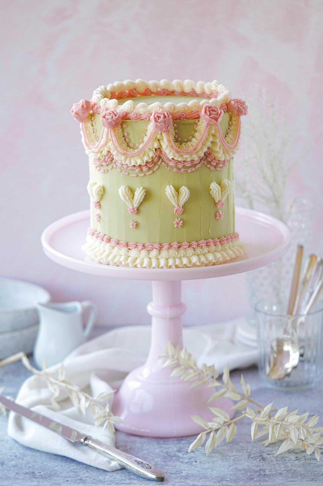 Vintage buttercream cake with pink and ivory piping, rose details, and decorative swags on a pink cake stand.