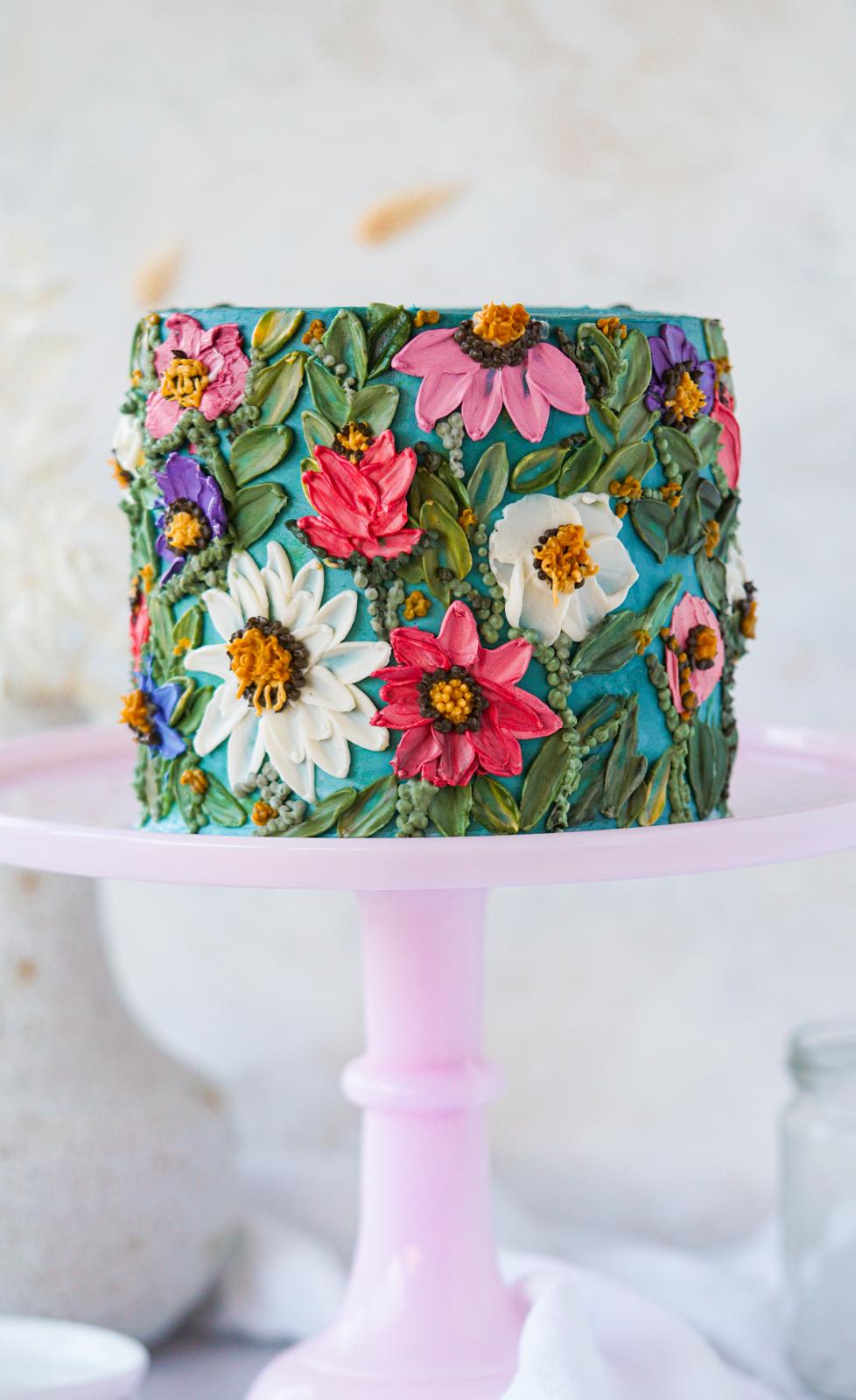 Teal buttercream cake with pink, white, purple, and red wildflower decorations on a pink cake stand.