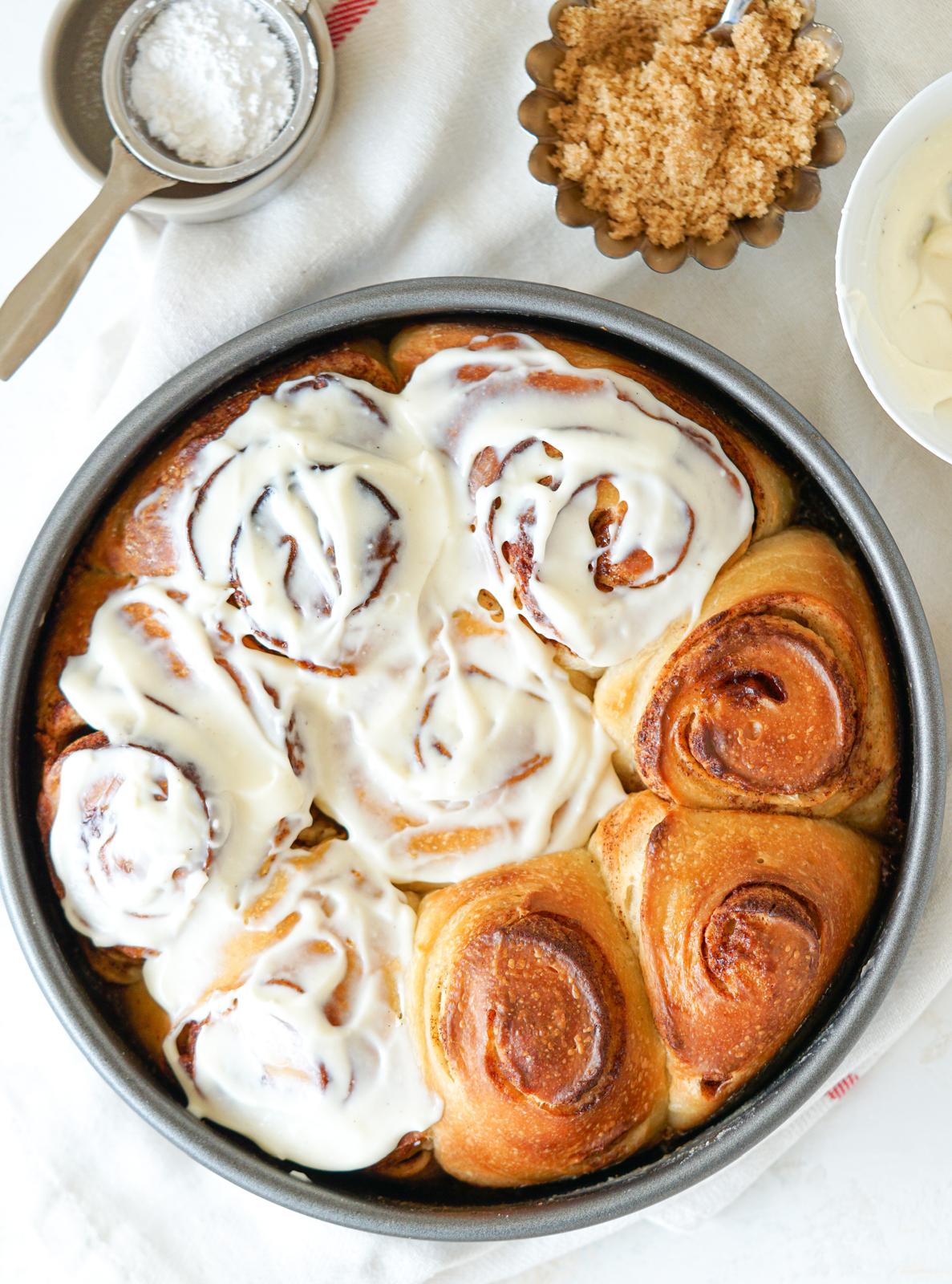Freshly baked cinnamon rolls in a round pan topped with cream cheese frosting.