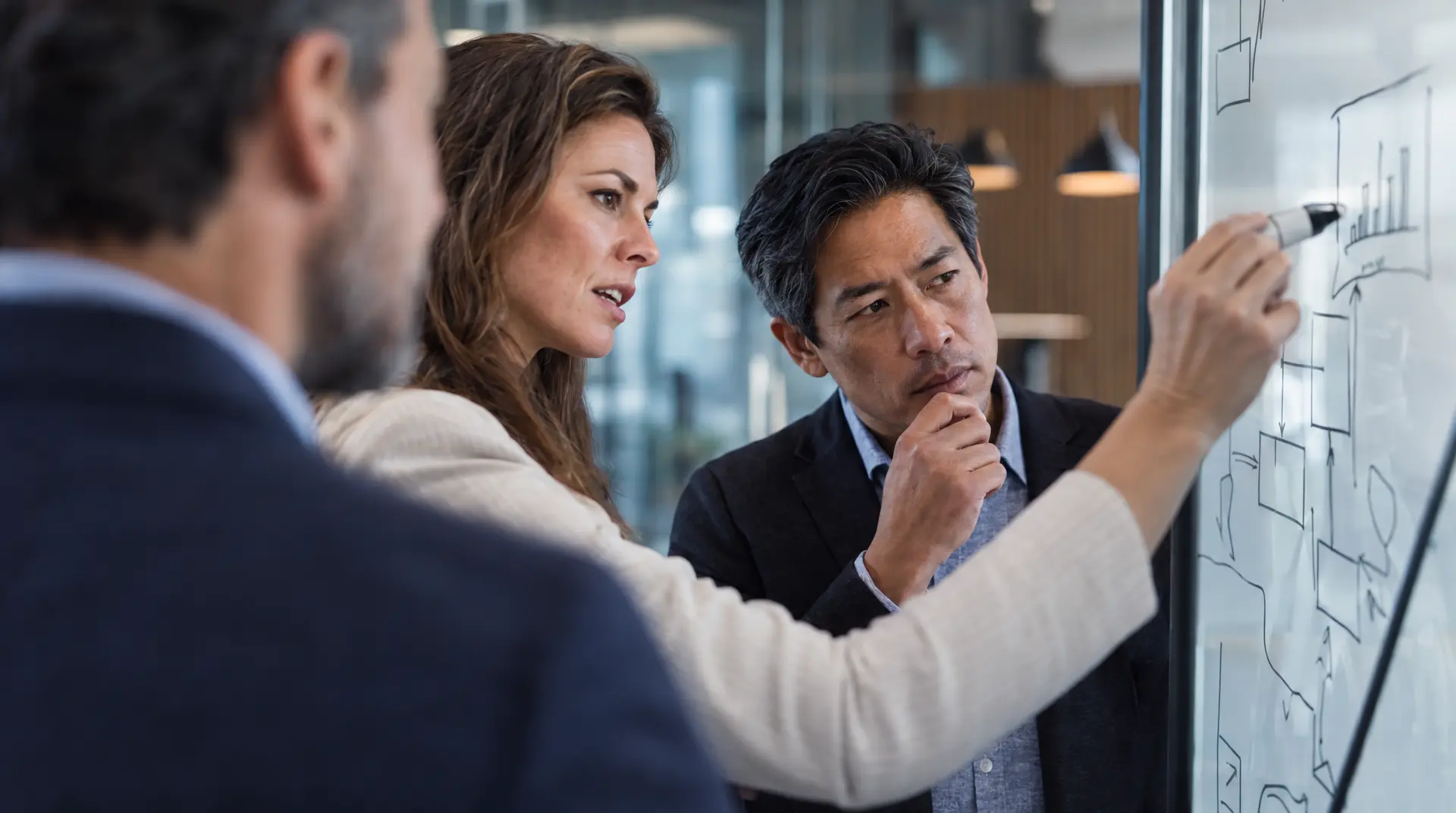 Two professionals review whiteboard diagrams in an office setting, supporting procurement roi and contract management discussions with a focused planning posture.