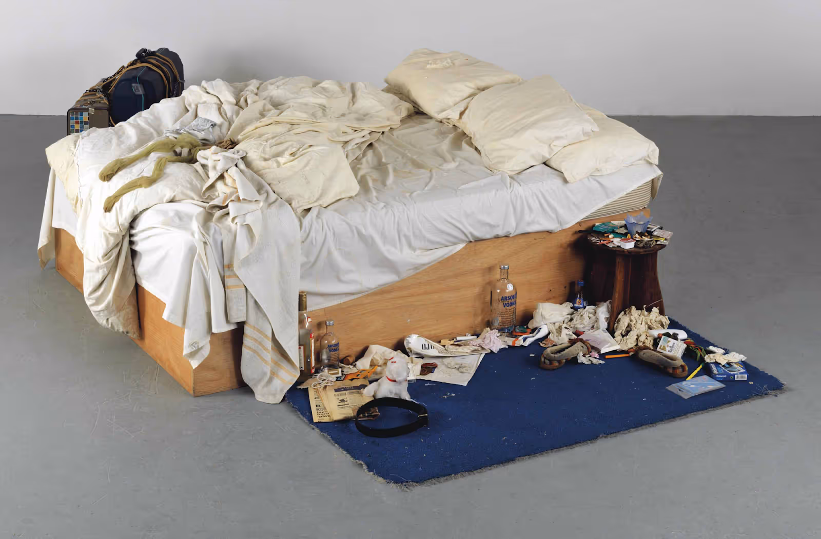 An unmade messy bed with bottles on the floor