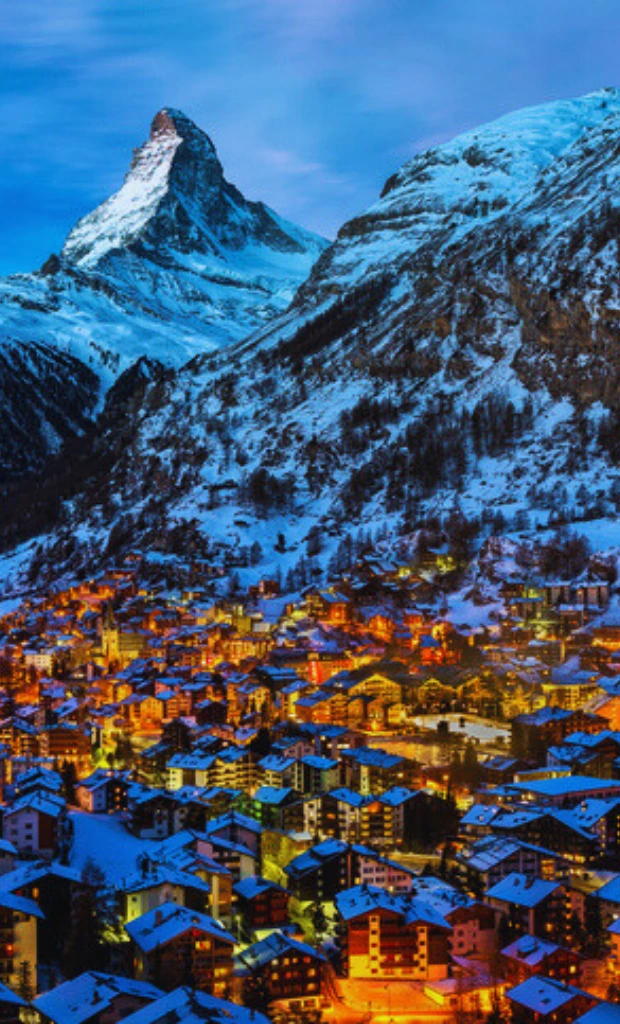 Village alpin suisse illuminé au pied des montagnes enneigées, avec chalets et station de ski en hiver.