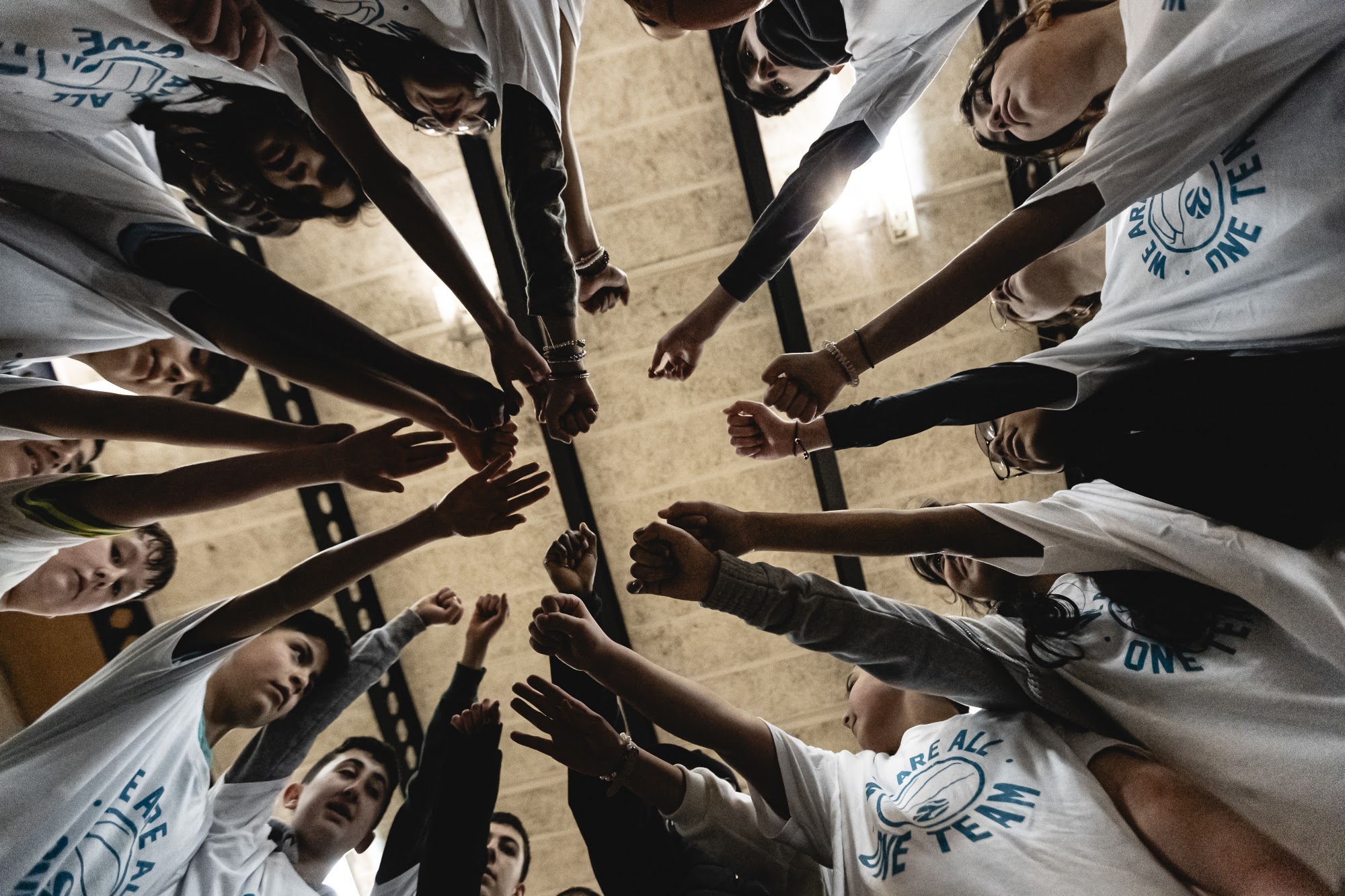 Young people hands in a huddle wearing One Team shirts