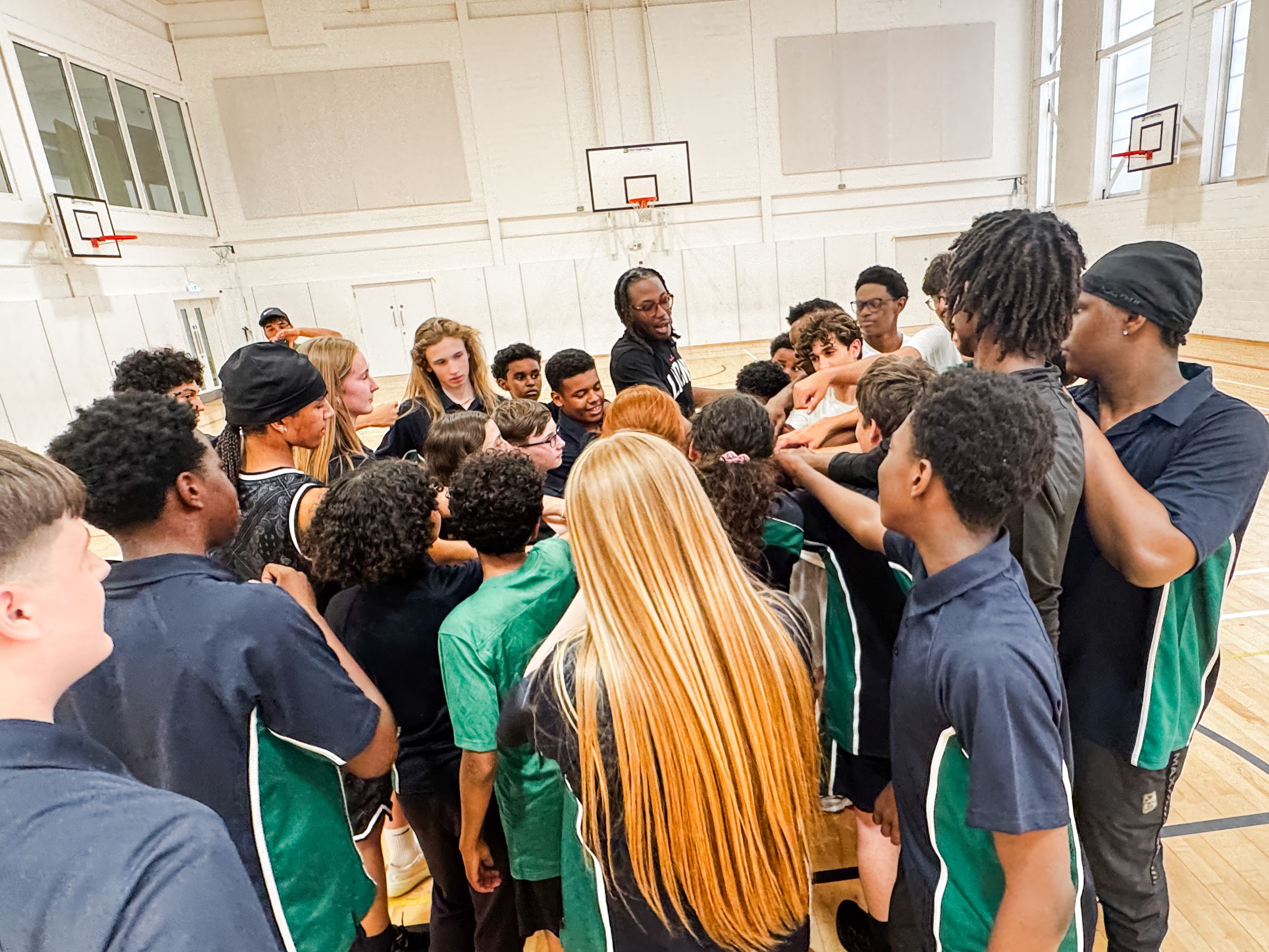 A London Lions coach leading a huddle with a group of school students in a sports hall