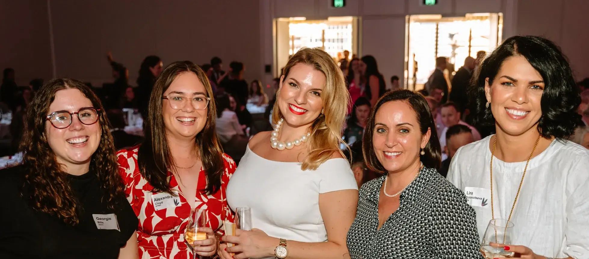 A group of WIRQ members posing at a networking event, holding drinks and smiling as they gather in a function room.