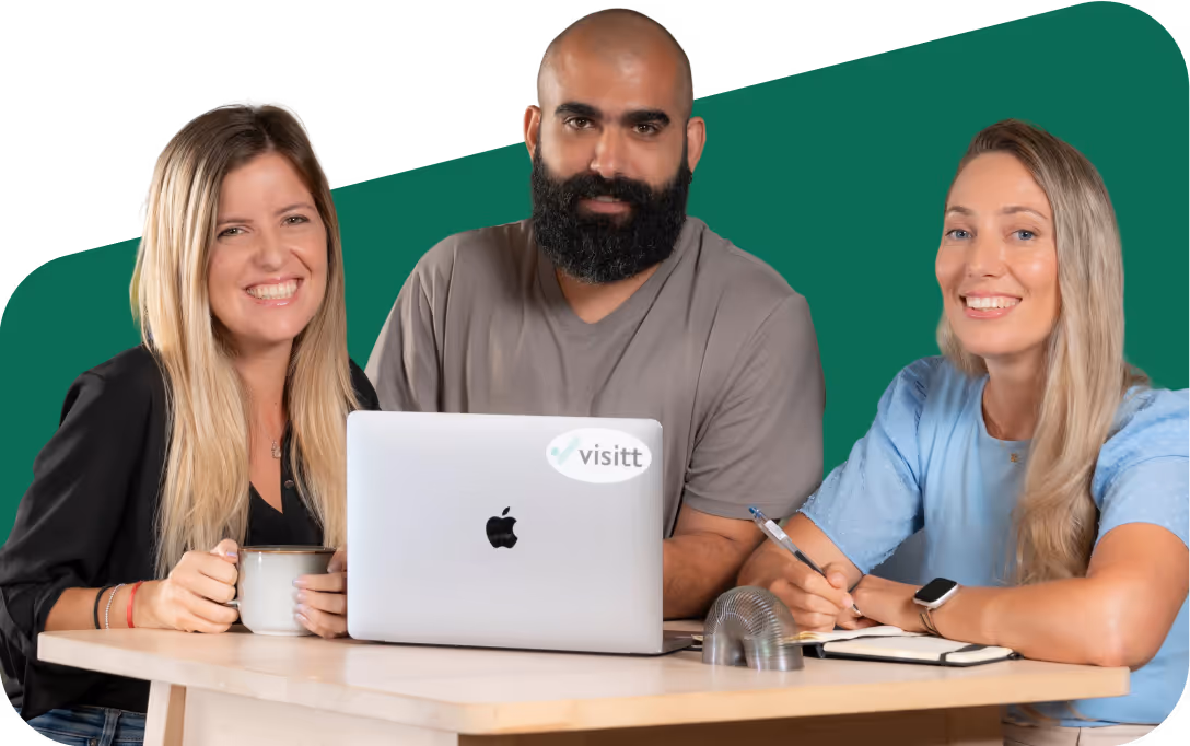 Three smiling people sitting at a table with a laptop; two women on each side and a bearded man in the center.
