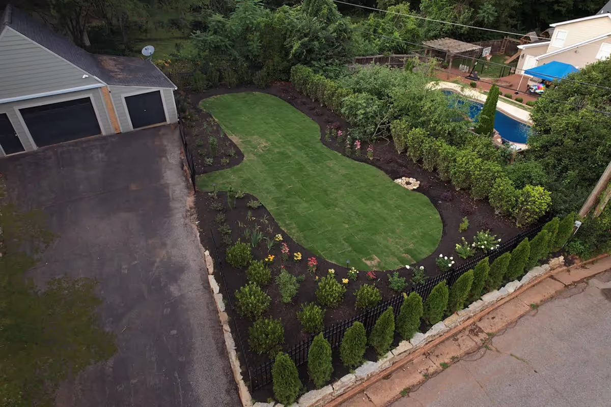 Aerial view of a luxury backyard landscape in South Carolina showcasing native plants around a neatly trimmed lawn and a swimming pool, emphasizing sustainable and aesthetic gardening practices.