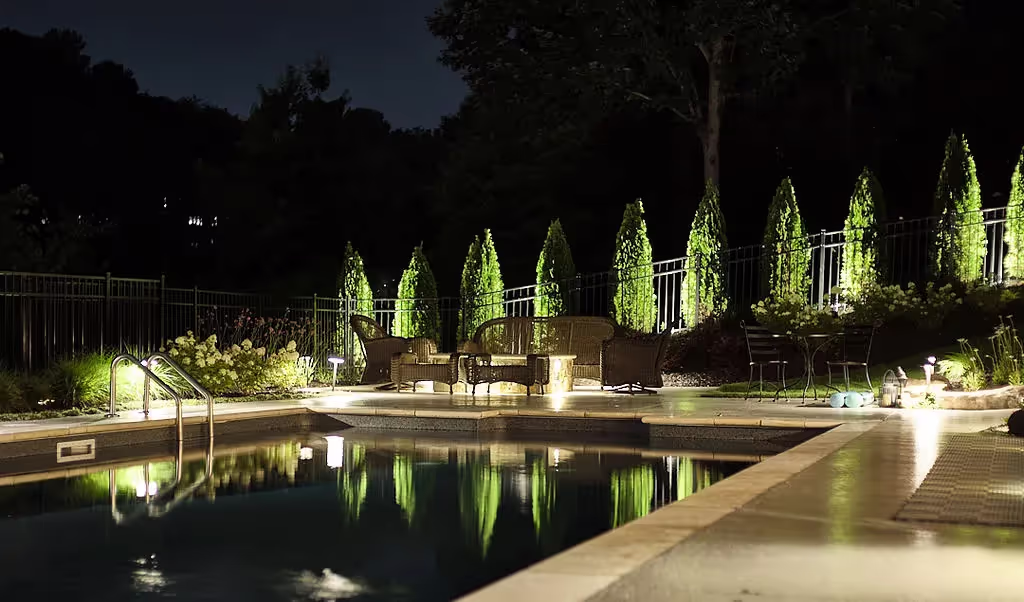 night time picture of a pool with outdoor lights lighting up the trees and walkways