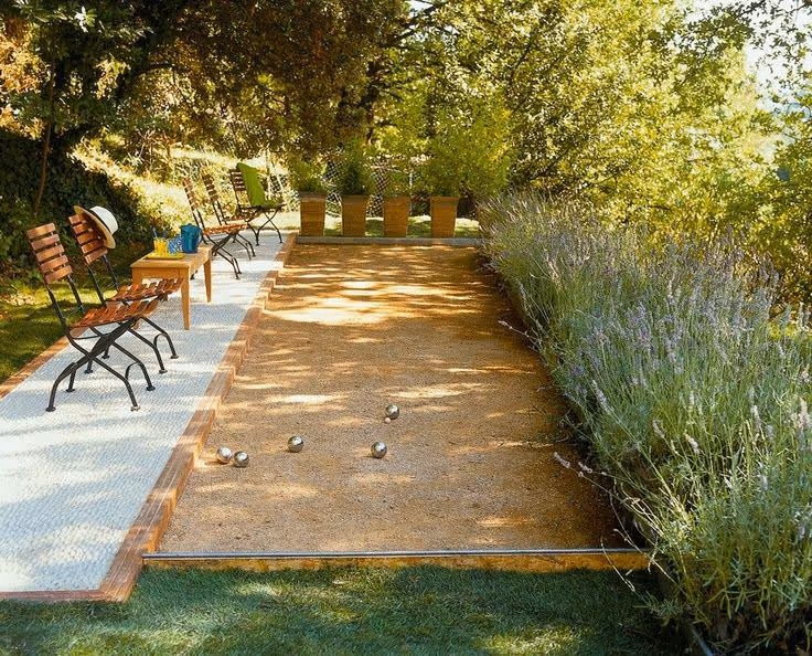 Child playing bocce ball on a grassy lawn, colorful bocce balls visible in the distance, bright daylight, casual outdoor setting.