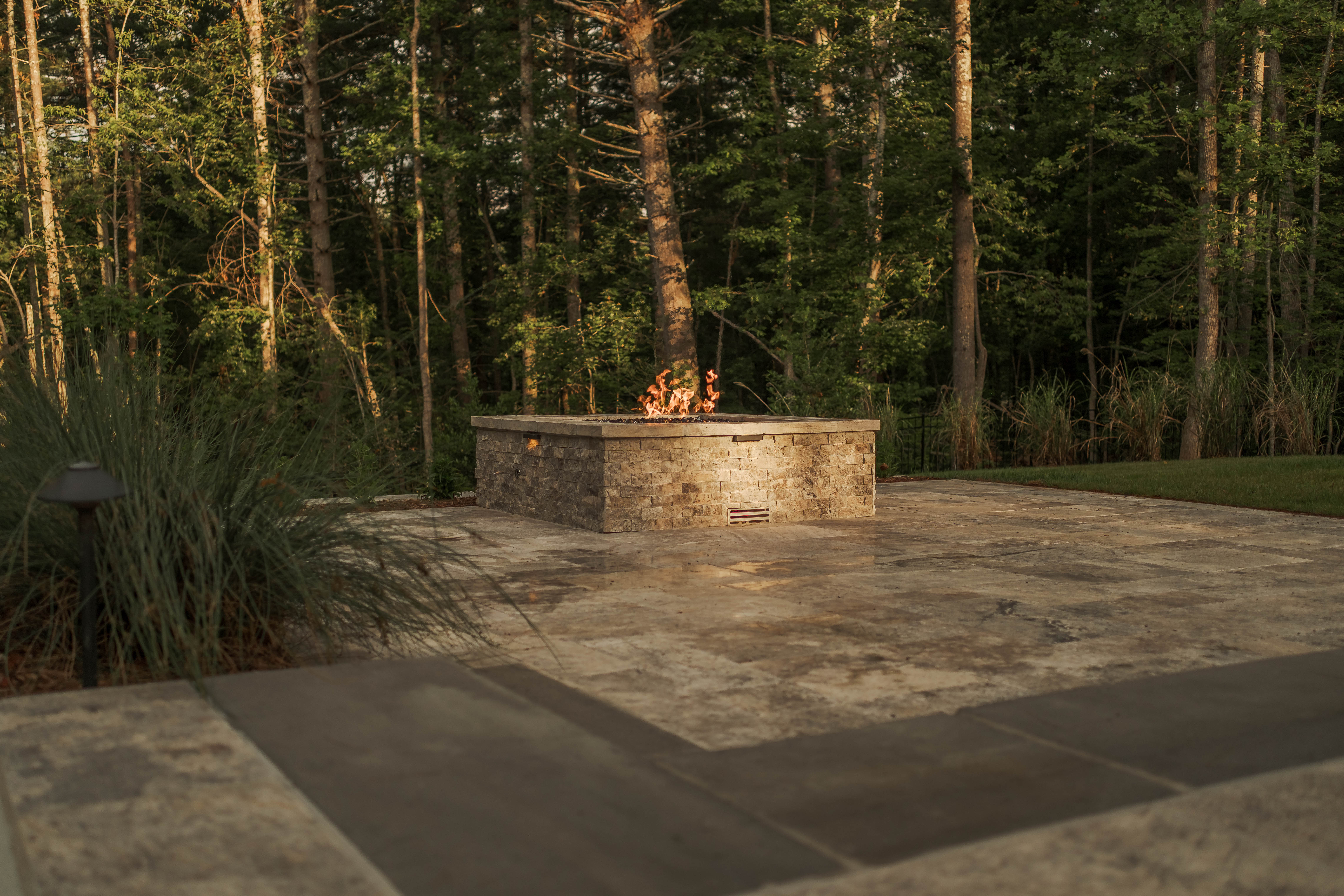 Custom backyard hardscape with paver patio, stone walkway, and built-in fire pit