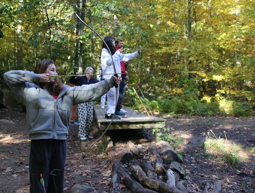 A girl practising archery in the forest at camp