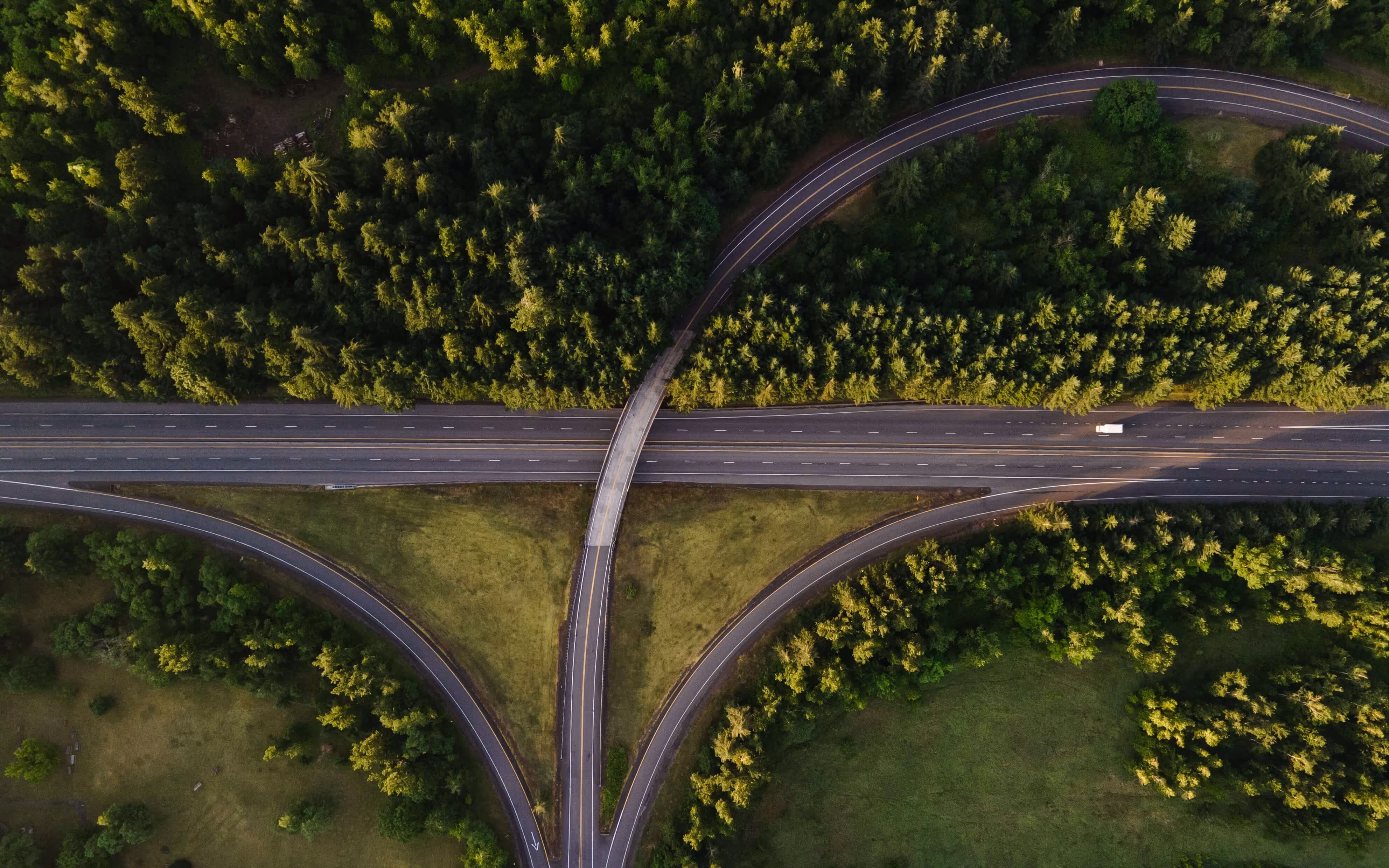 Luftaufnahme eines Autobahnkreuzes, umgeben von dichtem grünem Wald und Grasflächen.