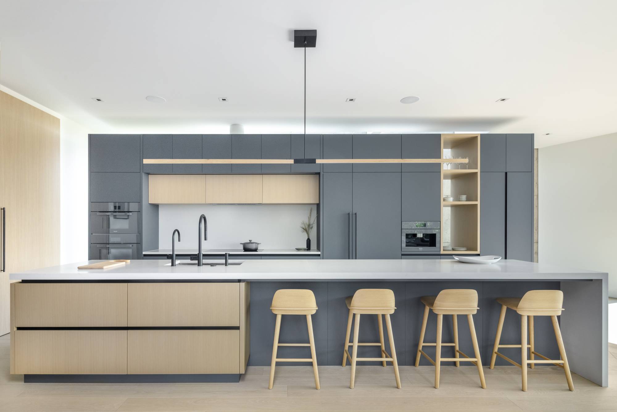 Barnero modern floating magic barn door in white oak veneer finish with a black linear door pull.  Gray and oak kitchen cabinetry.