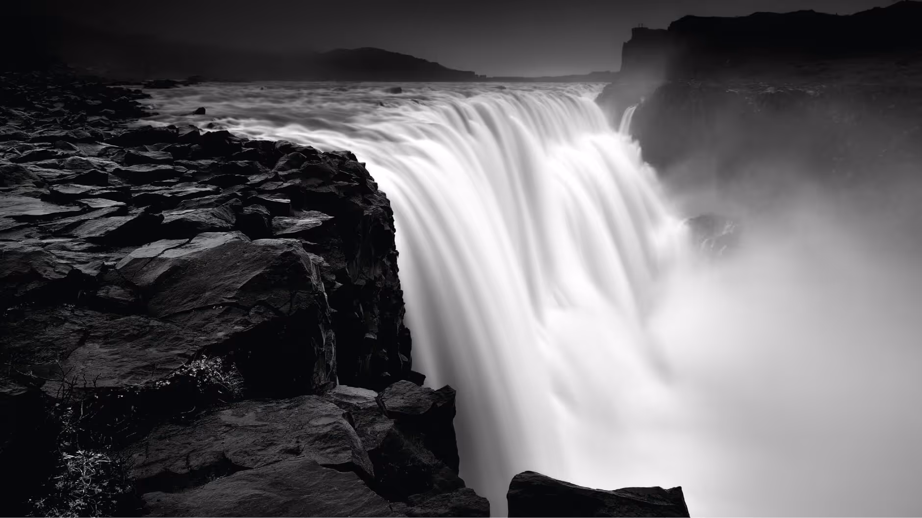 Black and white image of a powerful waterfall cascading over rocky cliffs with mist rising.