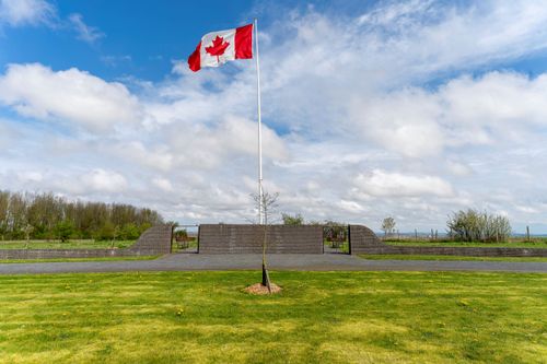The Centennial Park Flagpole flying the canadian flag against a blue sky, in the verdant green centennial park, with pebbled paths