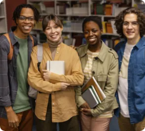 Four diverse university students standing together indoors holding books and smiling at the camera.
