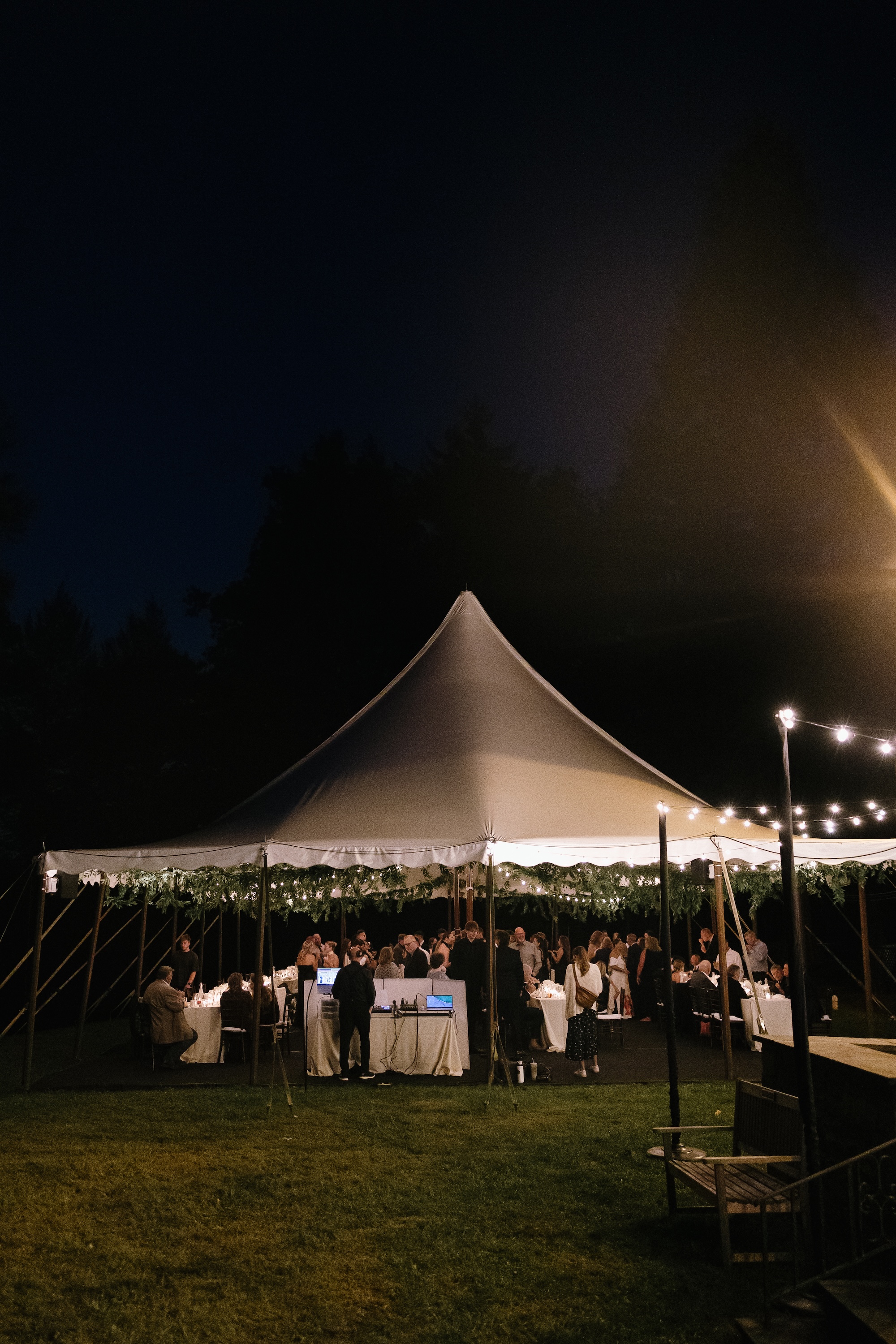 Guests mingling under a reception tent with string lights glowing beneath the night sky.
