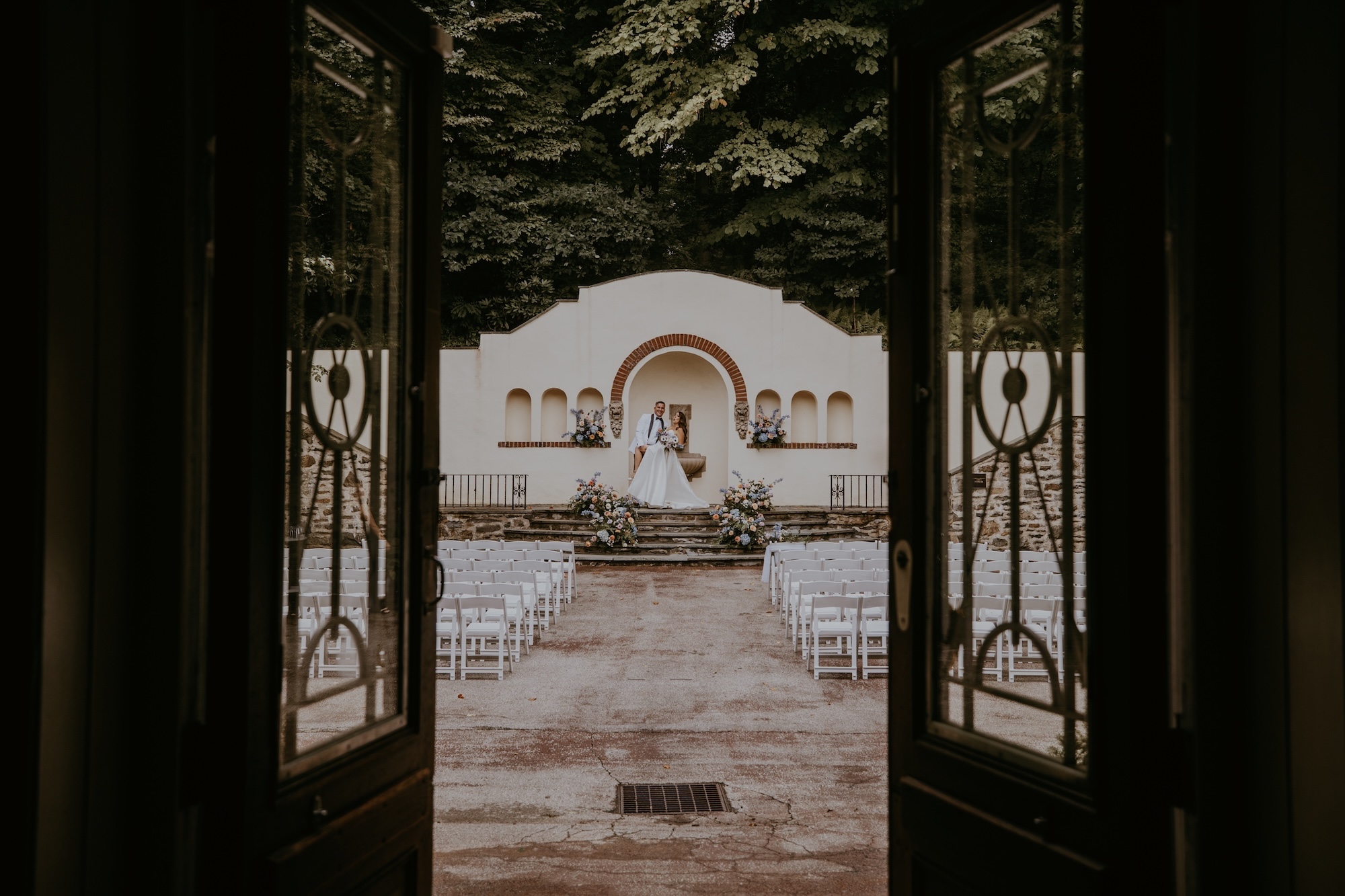 The mansion entrance doors propped open, revealing the bride and groom facing each other at the altar in the background.