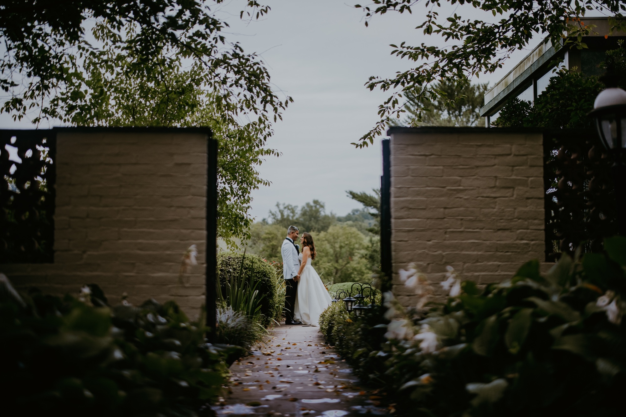 The bride and groom facing each other intimately in the distance, viewed through the garden gate in the foreground.