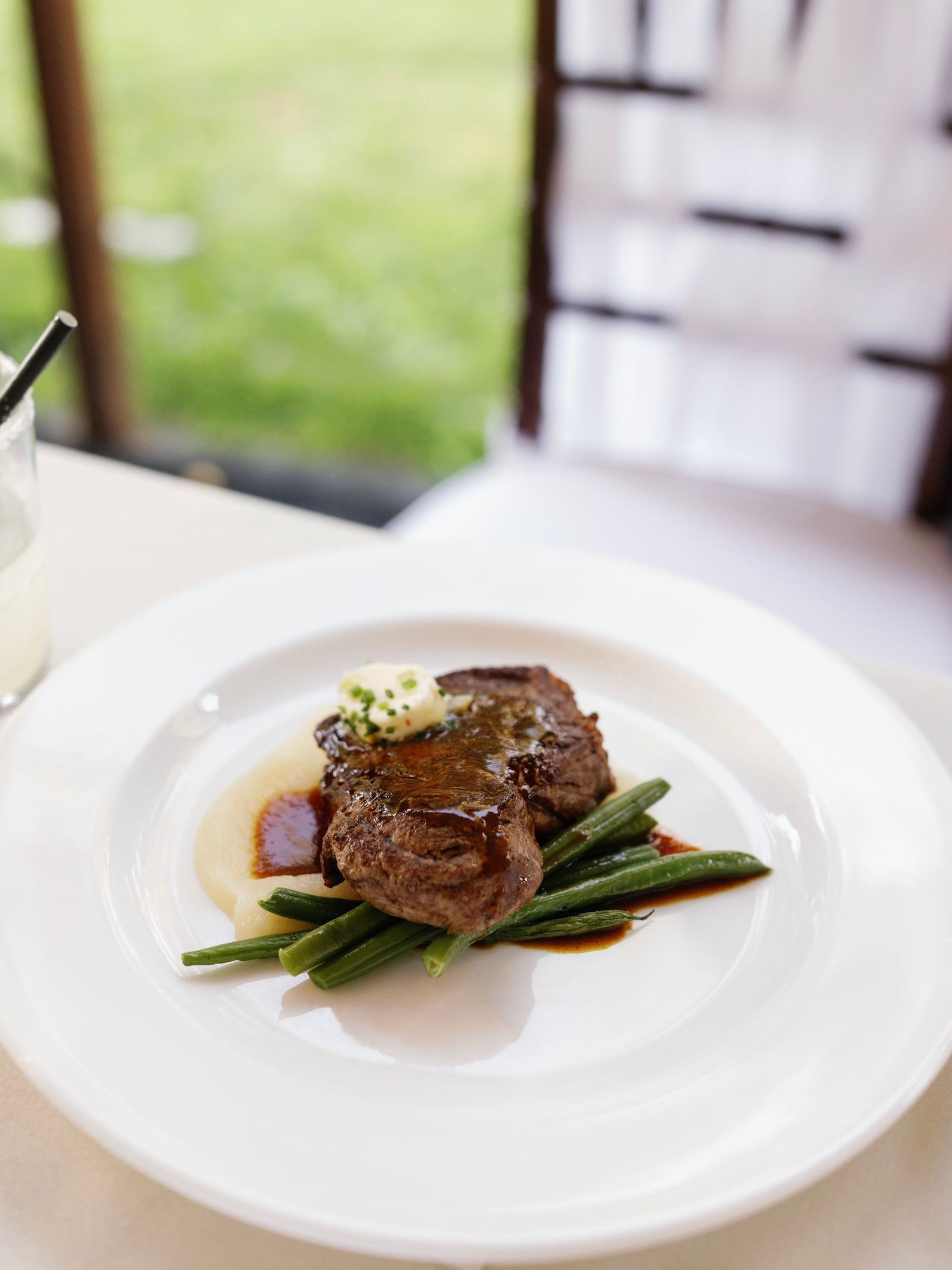 A plated steak entrée served with green beans, mashed potatoes, and herbed butter.