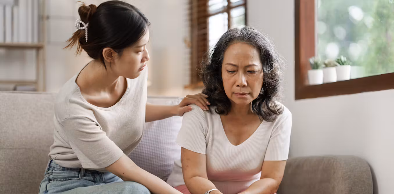 Une jeune femme réconforte une femme plus âgée assise sur un canapé, montrant de l'empathie et du soutien.