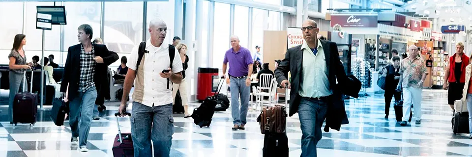 Des personnes marchant avec des bagages dans un terminal d'aéroport lumineux et animé avec des magasins et des coins salons en arrière-plan.