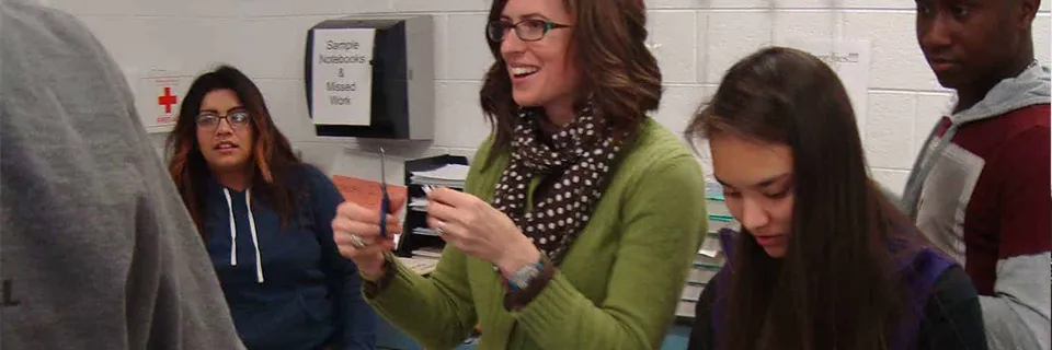 Un groupe d'élèves dans une salle de classe, écoutant attentivement leur professeur, qui explique un concept avec un outil à la main. Les élèves sont engagés et concentrés, leurs expressions reflétant leur curiosité et leur intérêt. L'enseignant est passionné et enthousiaste, rayonnant de chaleur et d'encouragement.