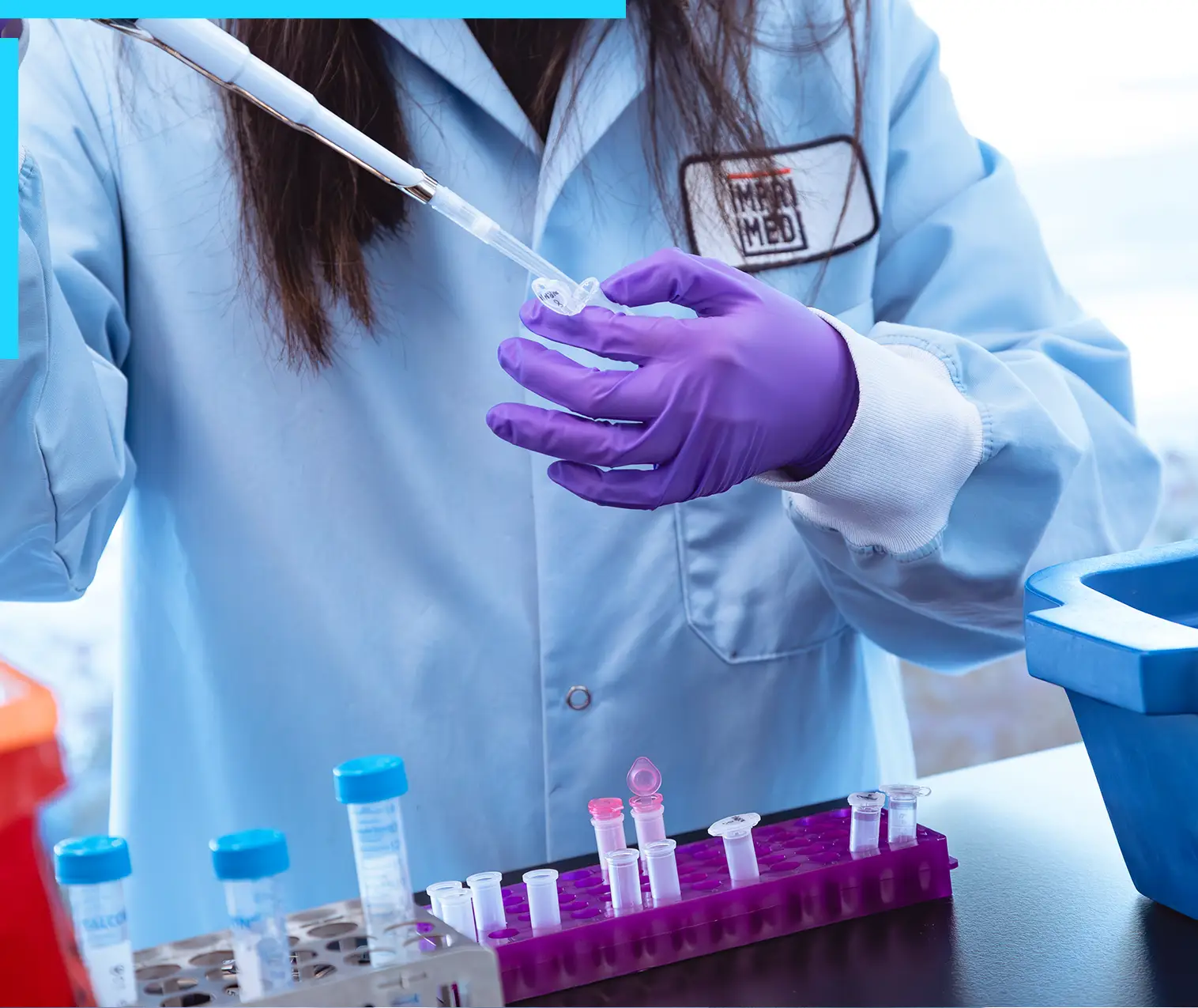 Scientist wearing purple gloves and a lab coat using a pipette to transfer liquid into a small test tube in a lab setting.
