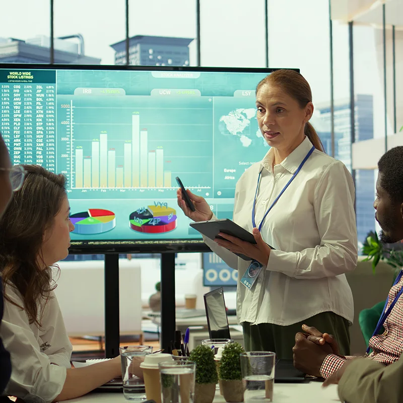 Businesswoman giving a presentation with digital charts to colleagues in a modern office.