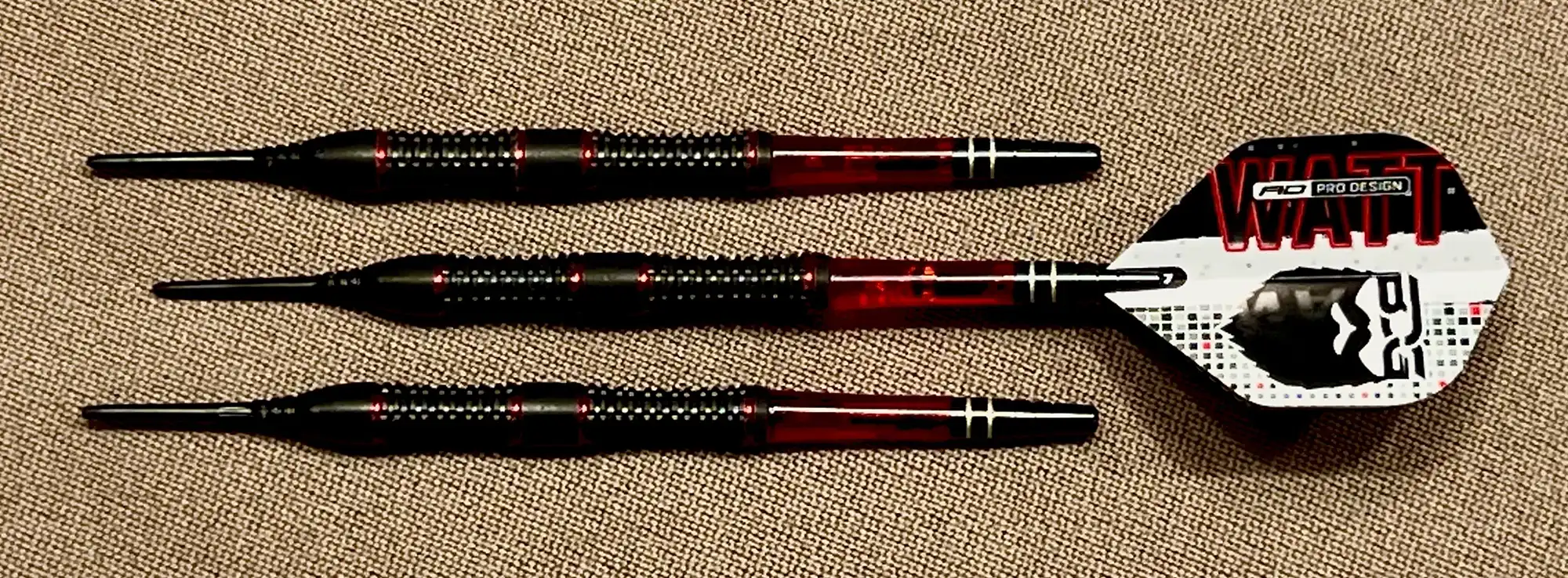 Three red and black darts with black-coated textured barrels. The flight is white with red accents and a black graphic of a monster face.