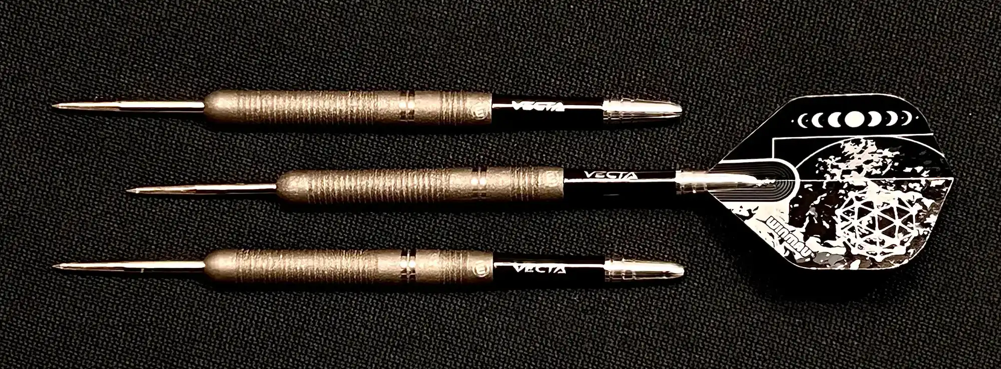 Three professional darts with textured bronze barrels and shiny silver points. A white and black dart flight with a moon phase design is attached.