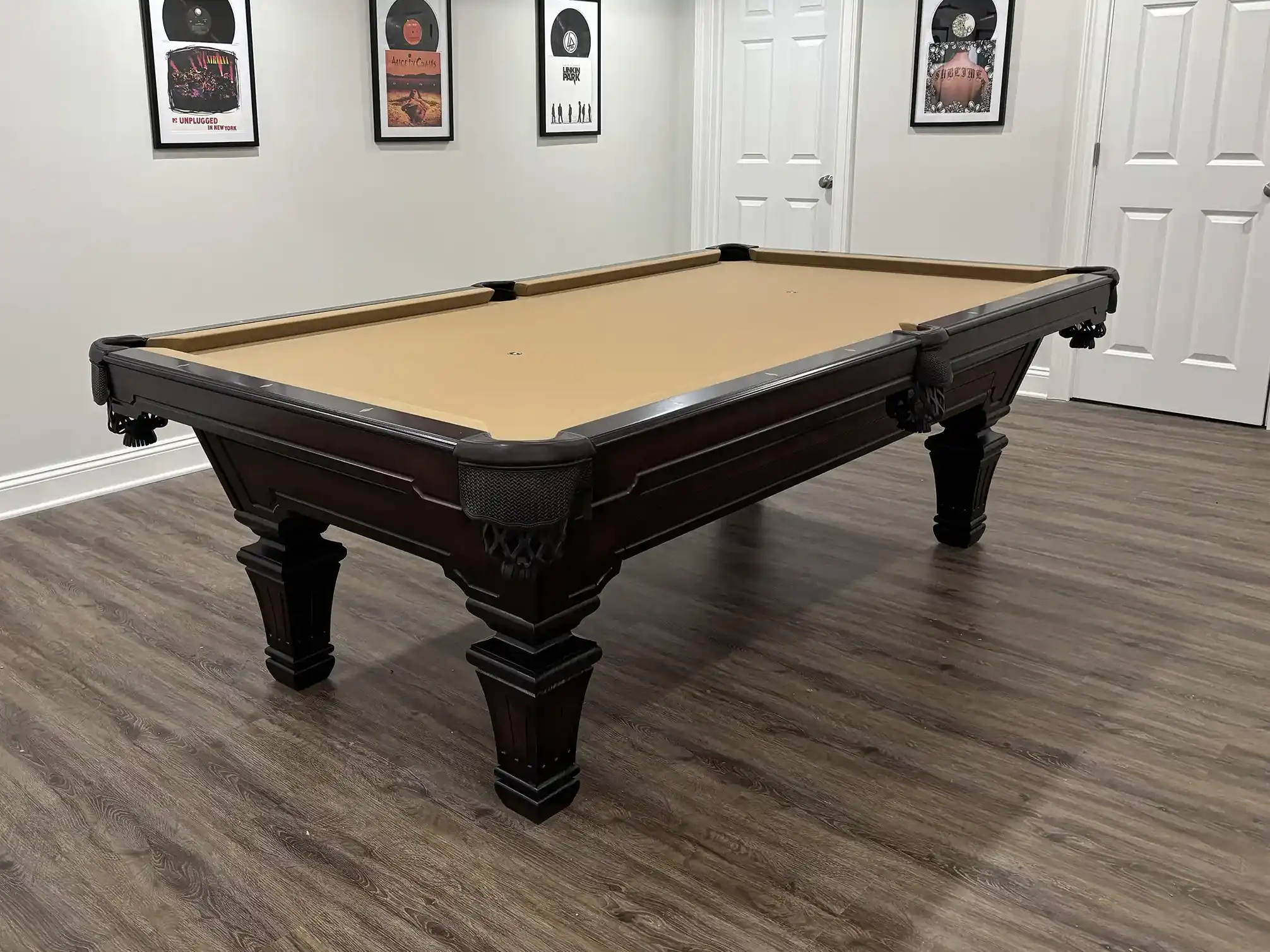 Classic dark wood Olhausen pool table with tan felt in a music-themed game room featuring framed record album art and wood floors.