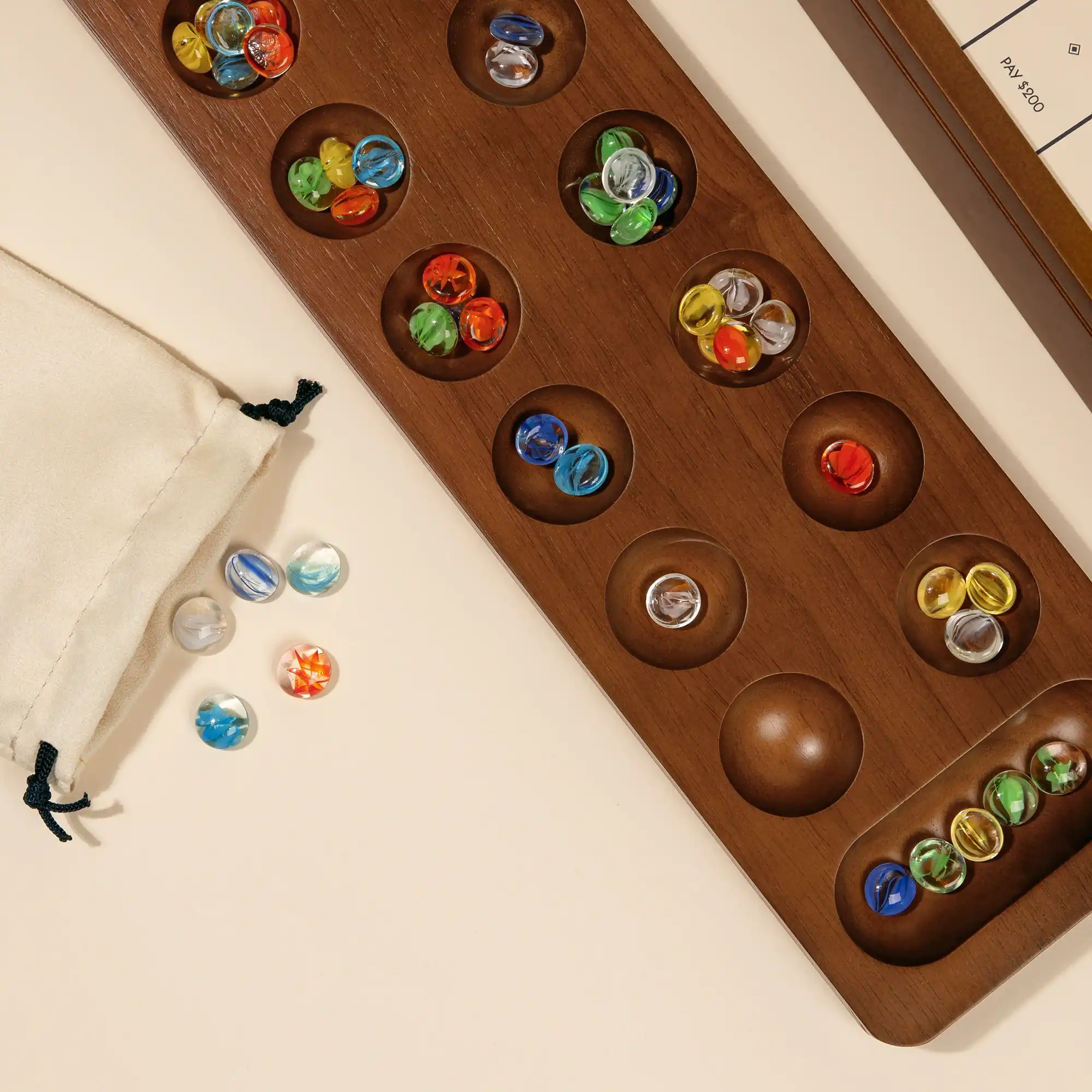 Close-up overhead view of a beautiful wooden Mancala board filled with colorful glass marbles, next to a small cloth pouch for marble storage.