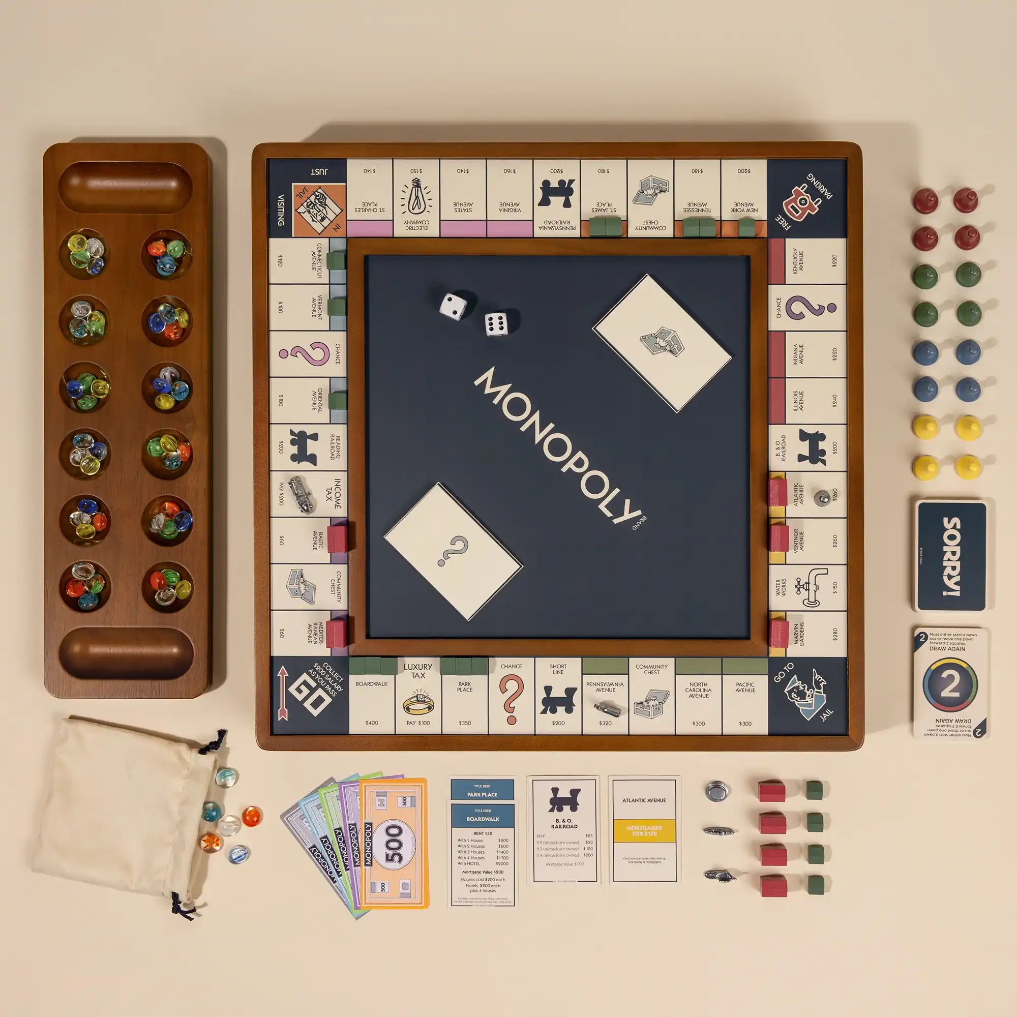 Flat lay image of a wooden board game set featuring a modern blue Monopoly board, a Mancala board with colorful marbles, and Sorry game pieces.
