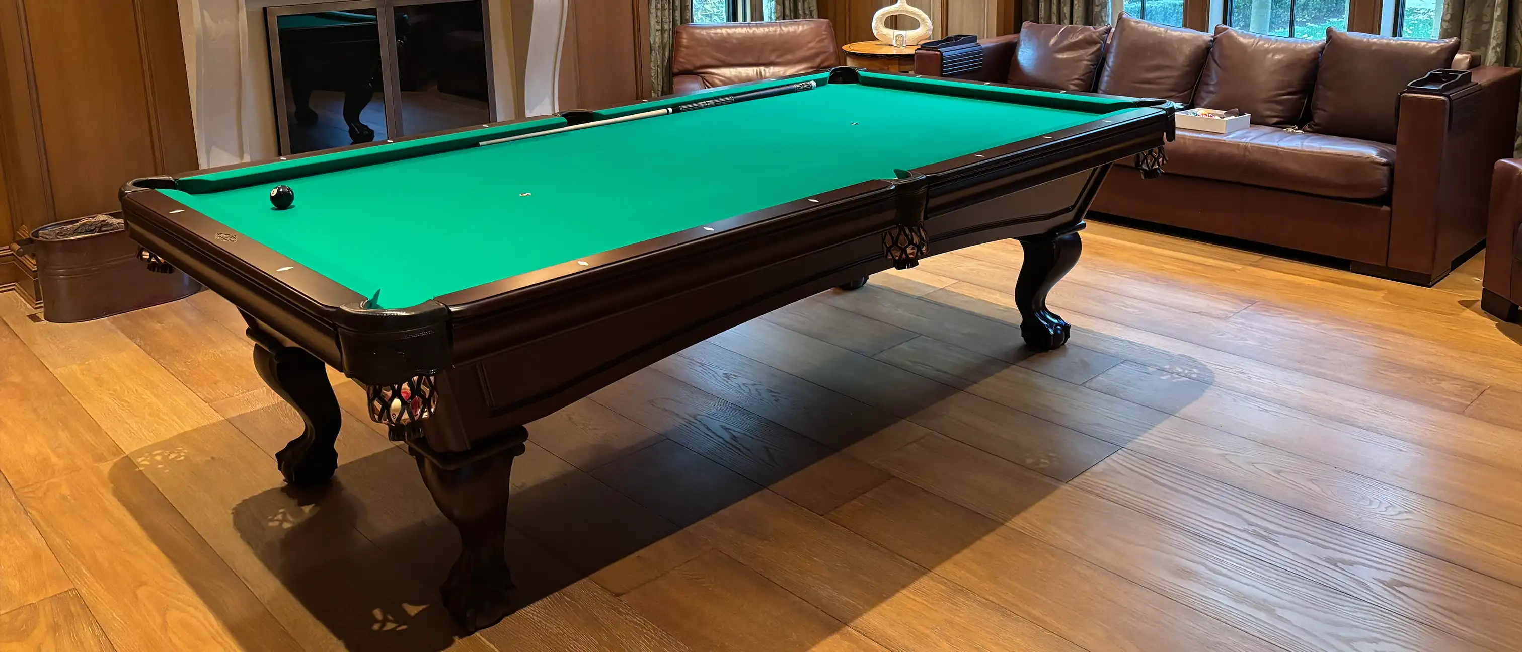 A luxurious billiard table with a green felt surface and dark wood finish sits on a hardwood floor in a cozy room.